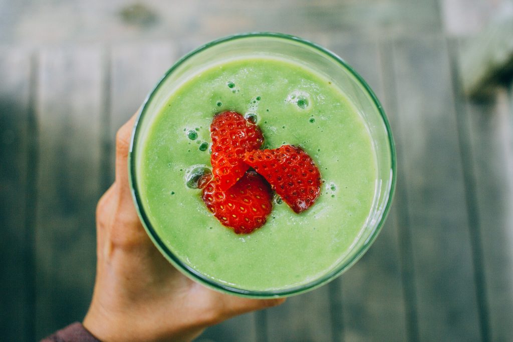 Female hold holding a green smoothie with sliced strawberries as a garnish