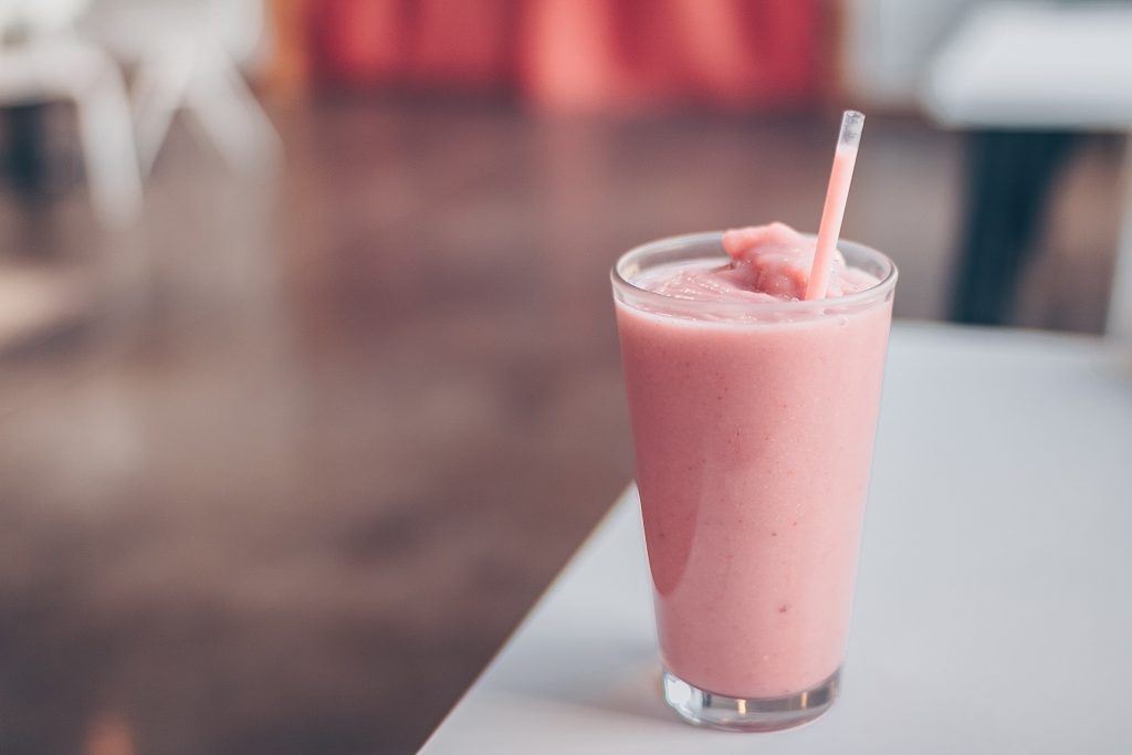 Pink smoothie in a glass with a straw on top of a table