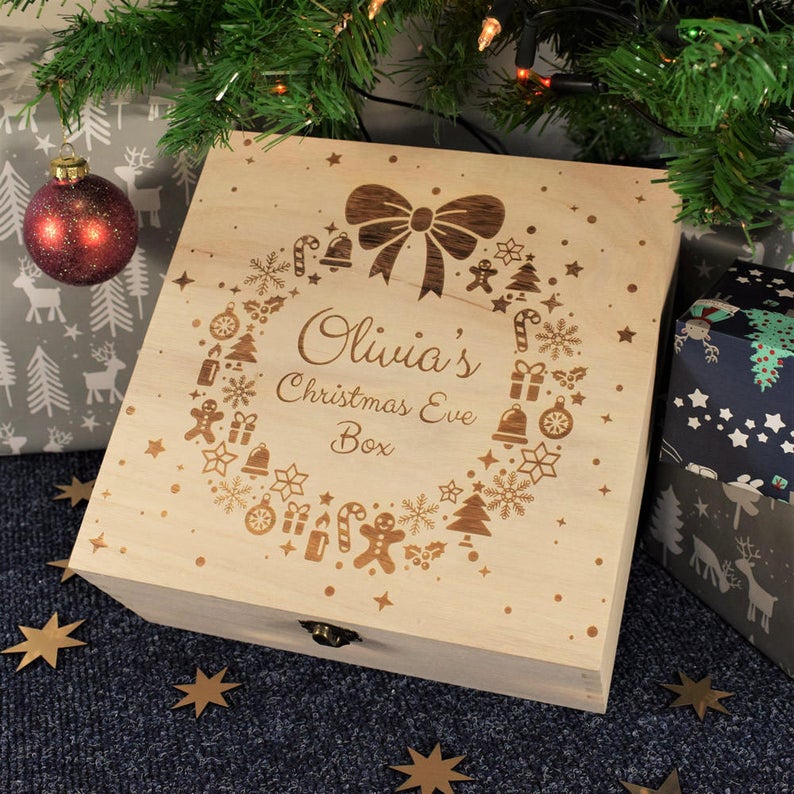 Wooden Christmas Box with Olivia's Christmas Eve Box engraved on it, background is a Christmas tree with presents and ornaments 